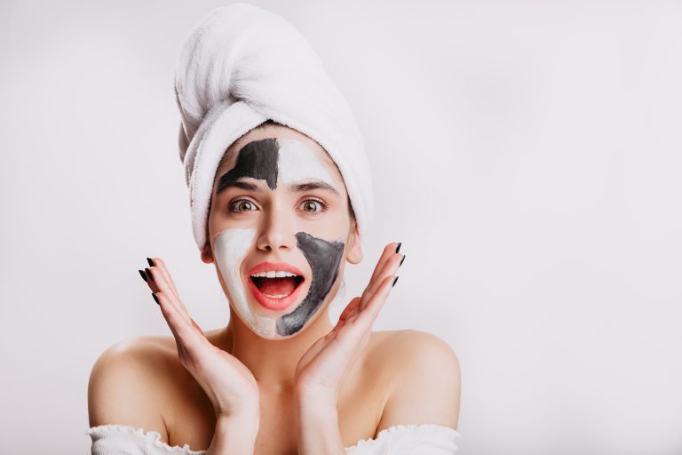 Joyful girl with face mask looks at camera in surprise. Green-eyed woman posing on white background after washing her hair.